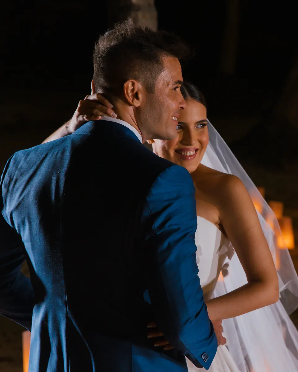 Thalita e Leonardo Medina abraçados à noite, na praia, diante de um caminho de lanternas na areia, no casamento deles