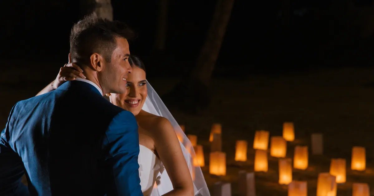 Thalita e Leonardo Medina abraçados à noite, na praia, diante de um caminho de lanternas na areia, no casamento deles