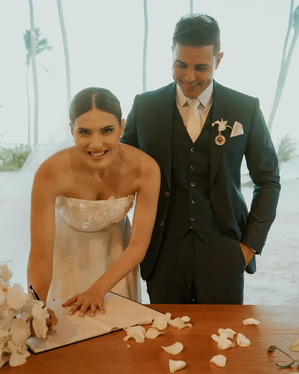 Thalita assina o livro na cerimônia do casamento dos Medinas, com o Leonardo ao lado, diante da praia