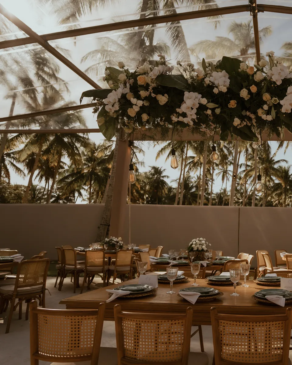 Salão da recepção do casamento dos Medinas, com mesas postas, arranjo floral suspenso e coqueiros ao fundo